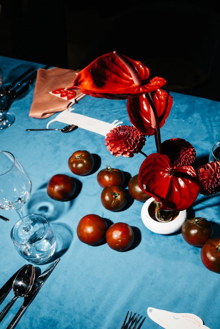 Dinner table set with red anthuriums and tomatoes on blue linen